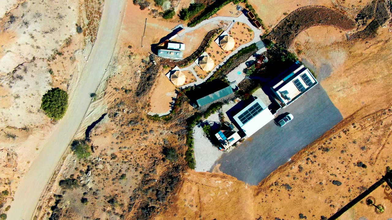 Aerial view of a building and parking lot in sandy desert terrain.