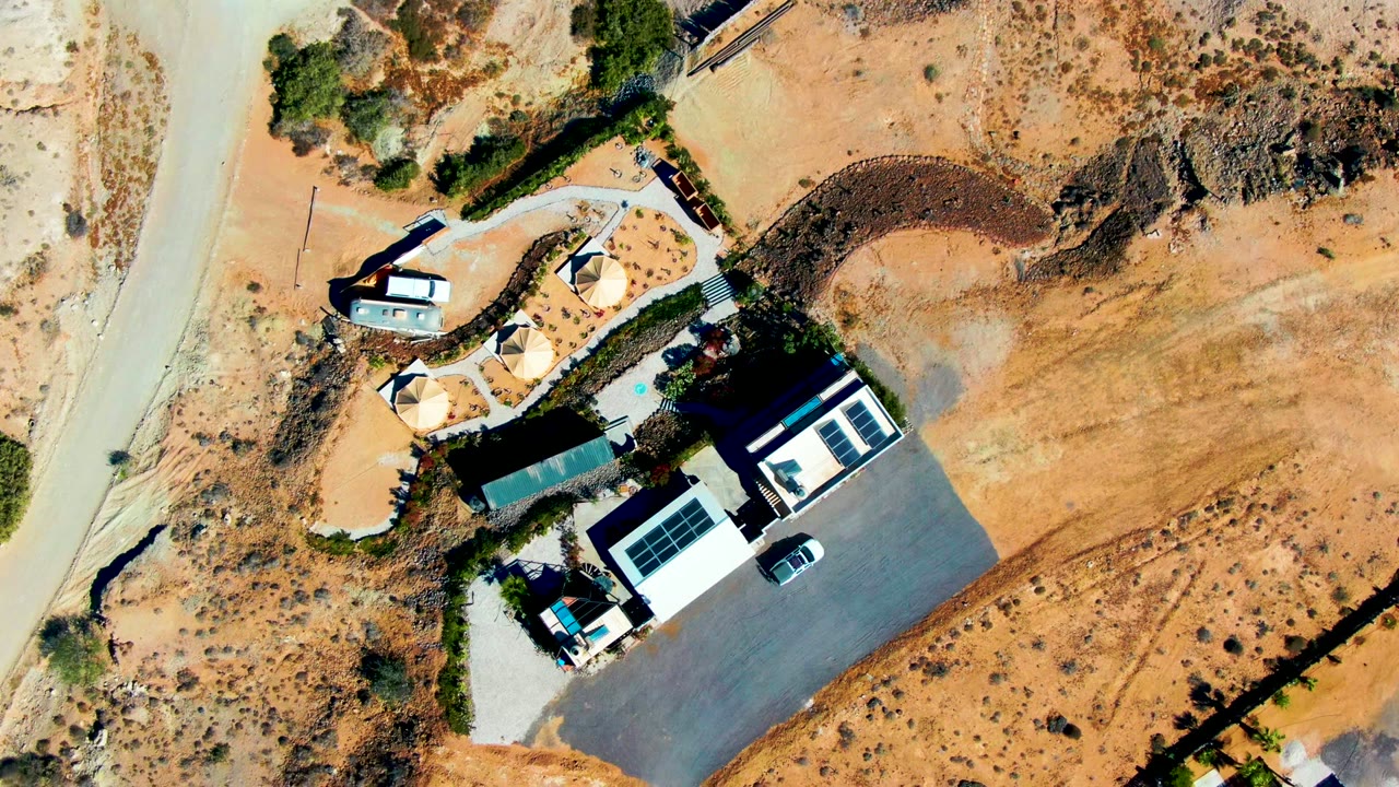 Aerial view of a white building with solar panels and desert road.