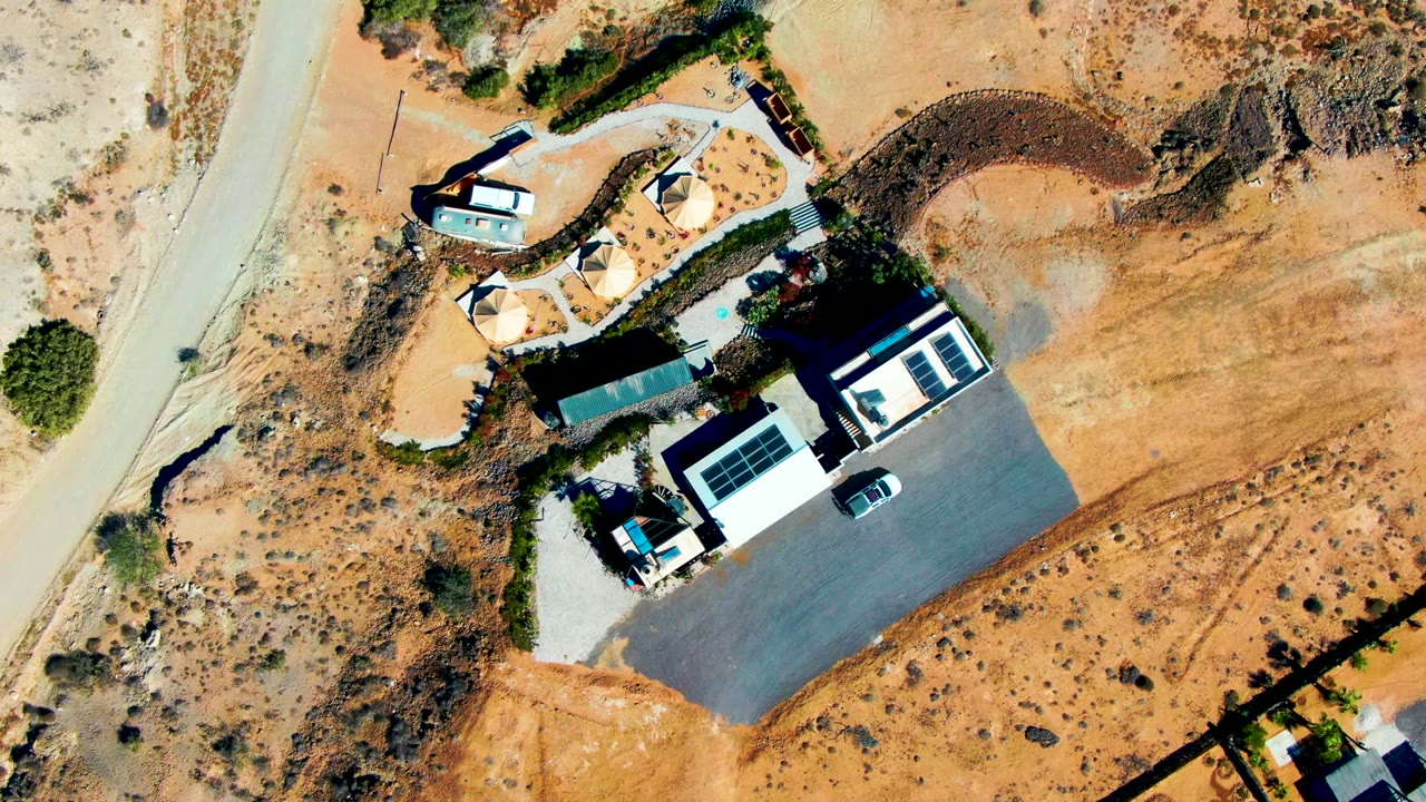 Top-down view of buildings, driveway, road, and dry vegetation.