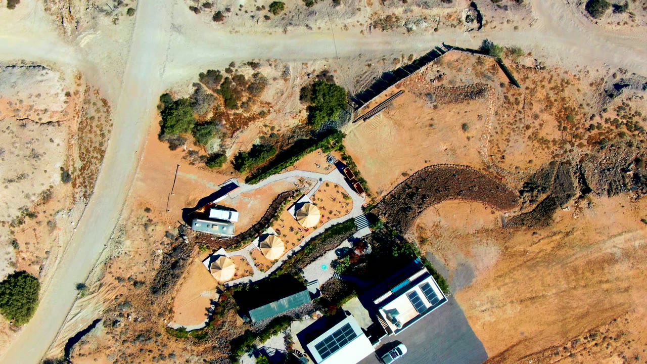 Aerial view of a vehicle near a curved dirt road by a house and driveway.