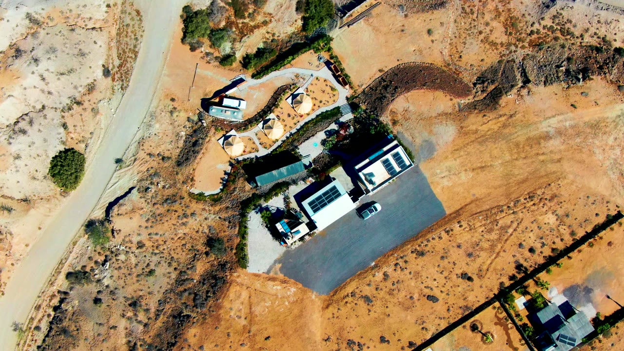 Top-down view of a desert home, driveway, parked car, and dry open lot.