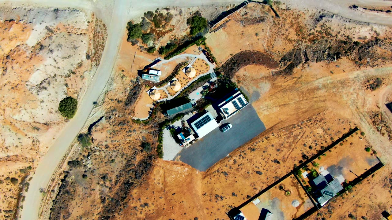 Top-down aerial view of modern homes, fenced lots, sandy desert ground, scrub vegetation, and no visible people in San Juanico, Baja California Sur.