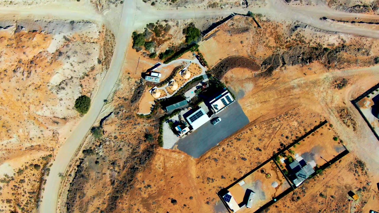Aerial view of small buildings beside pale dirt roads in dry terrain.