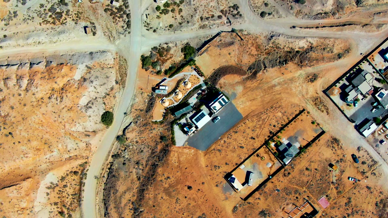 Aerial view of a car on a dirt road beside desert homes and open land.