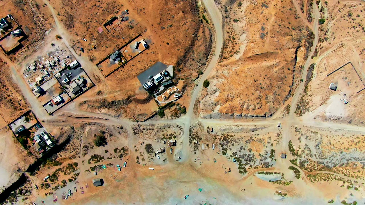 Top-down view of dirt roads, buildings, and sandy beach edge
