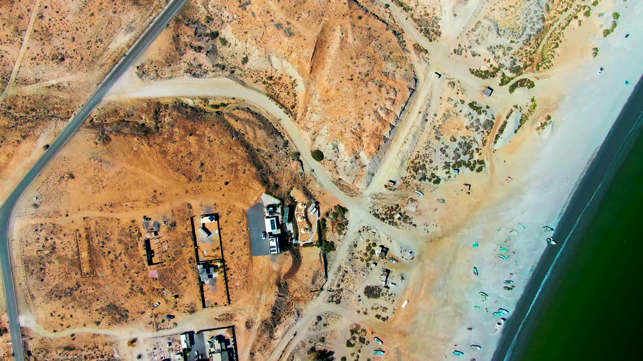 Aerial view of beachfront lots, small structures, beach umbrellas, and green shoreline water.