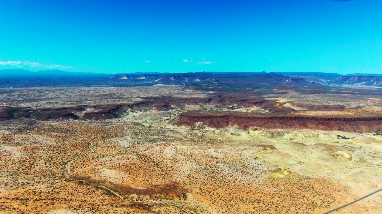 Aerial desert landscape with ridges, washes, and a road entering the lower right.