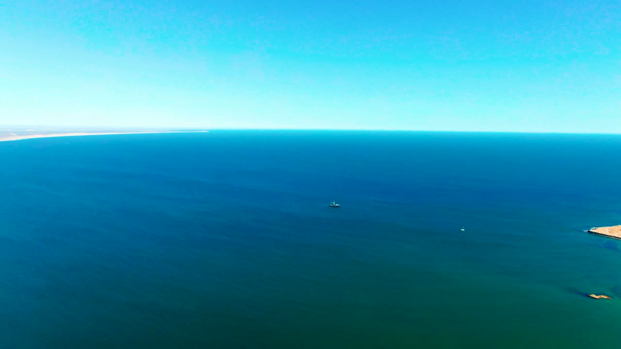 Open blue ocean with small distant boats and desert horizon