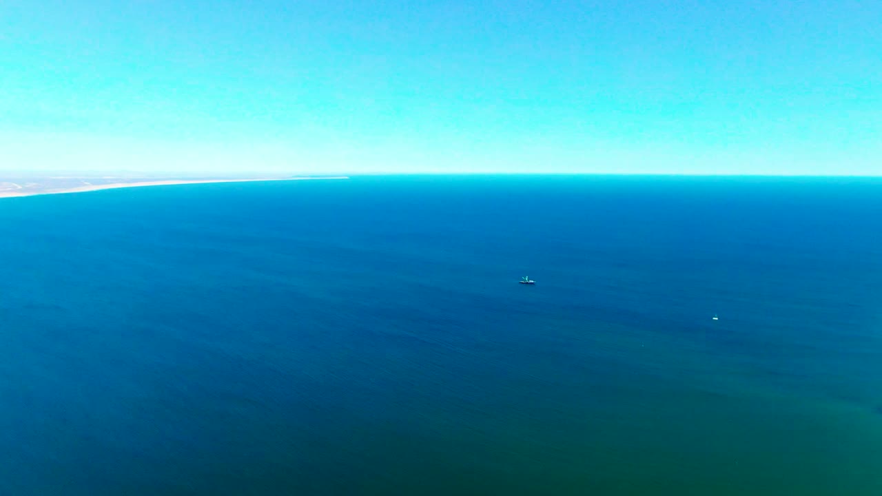 Wide aerial frame over San Juanico ocean water, with the coastline reduced to a thin strip near the upper left edge, clear sky, and no visible people.