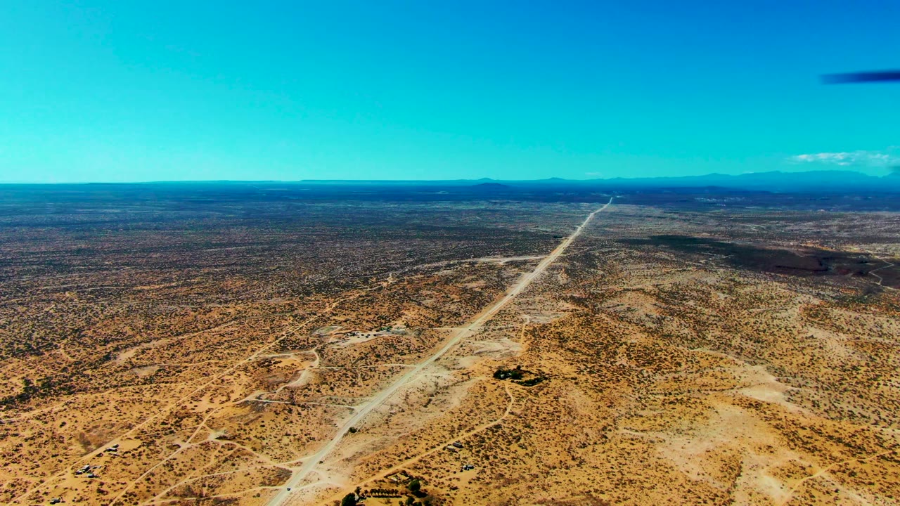 At 0:00, an aircraft-window view looks over San Juanico desert scrub toward a long dirt airstrip and distant mountains, with no visible people.
