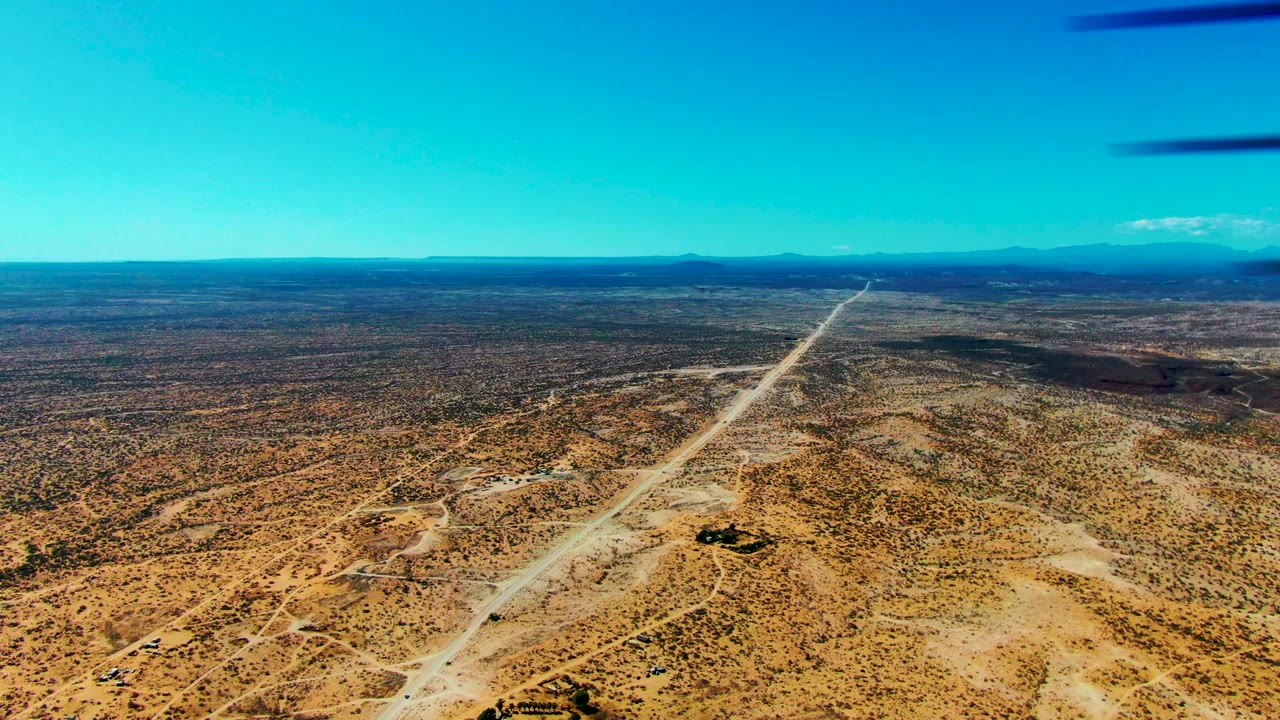 Dirt runway and sandy desert terrain seen from an aircraft with wing edge above.