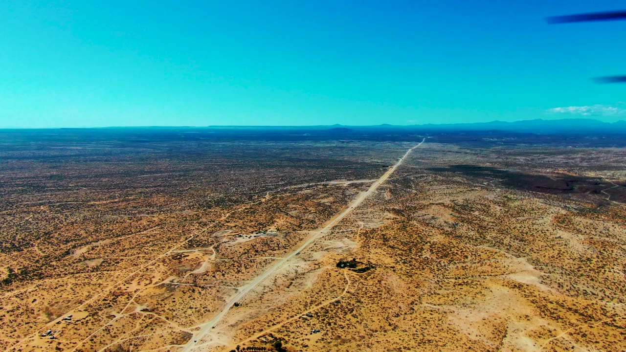 At 0:02, the San Juanico airstrip remains prominent across the scrubby desert floor while low mountains sit on the far horizon and no people are visible.