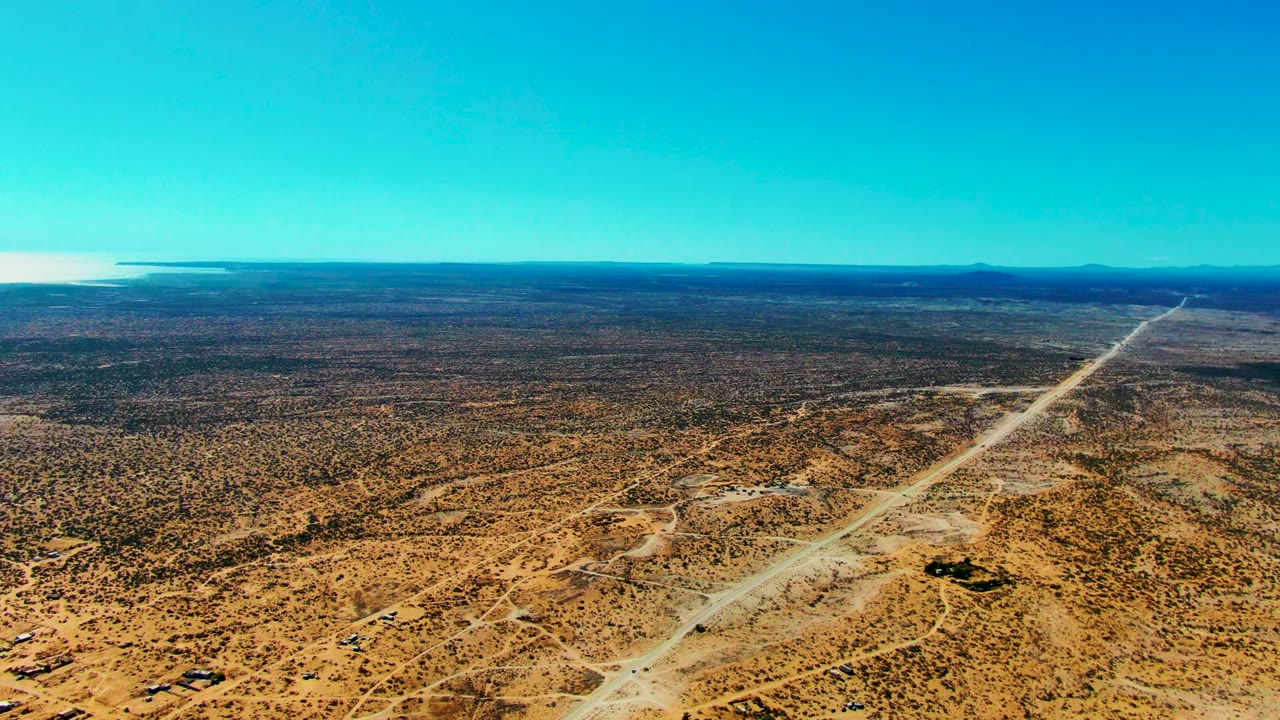 Aerial desert landscape with road lines and the ocean beginning to appear on the horizon.