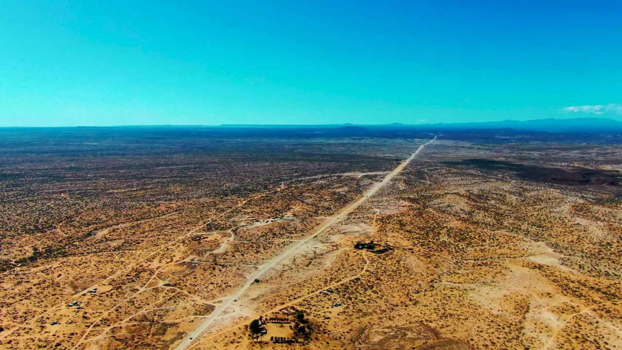 Opening aerial frame over San Juanico, Baja California Sur, with a pale dirt road cutting through sandy scrubland toward distant mountains and no visible people.