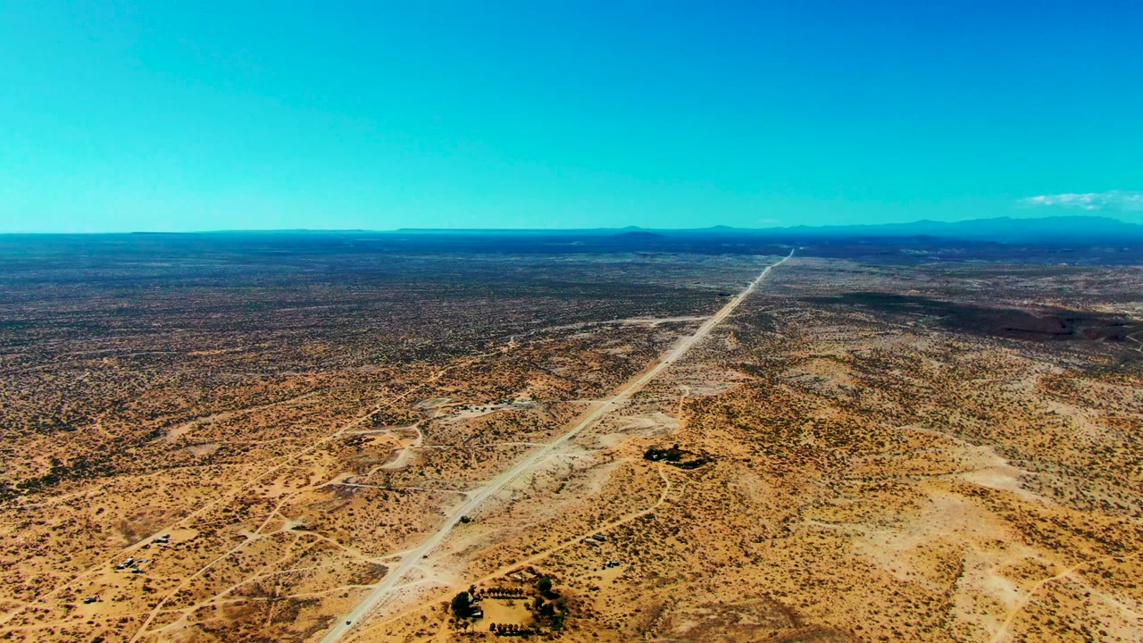 Long dirt road crossing dry desert beneath a clear blue sky.