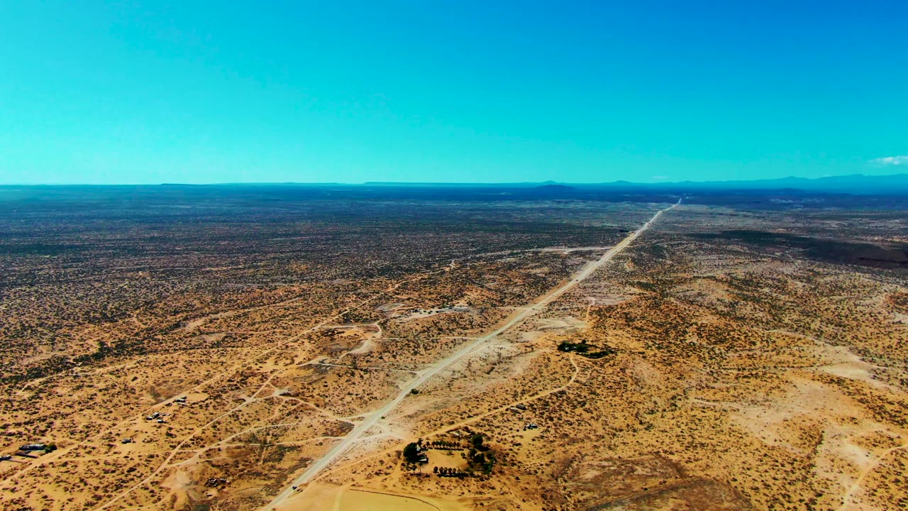 Opening aerial frame over San Juanico, Baja California Sur, showing a pale road crossing scrub desert toward a distant horizon with no visible people.