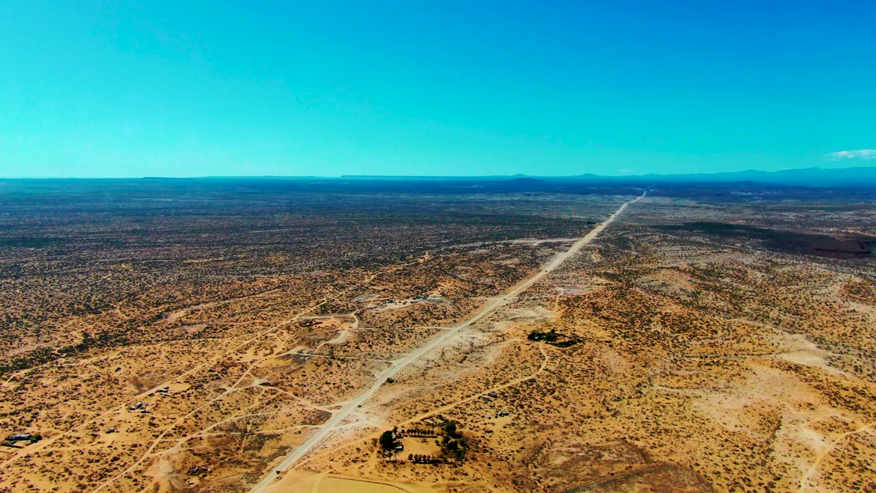 Aerial desert highway with sandy tracks and small structures near the road.