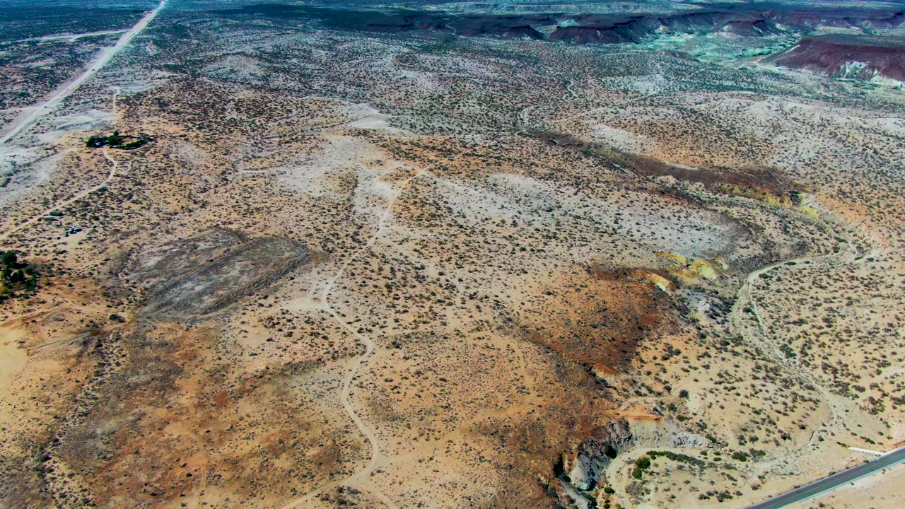 Wide aerial desert view with dirt road and distant mountains.