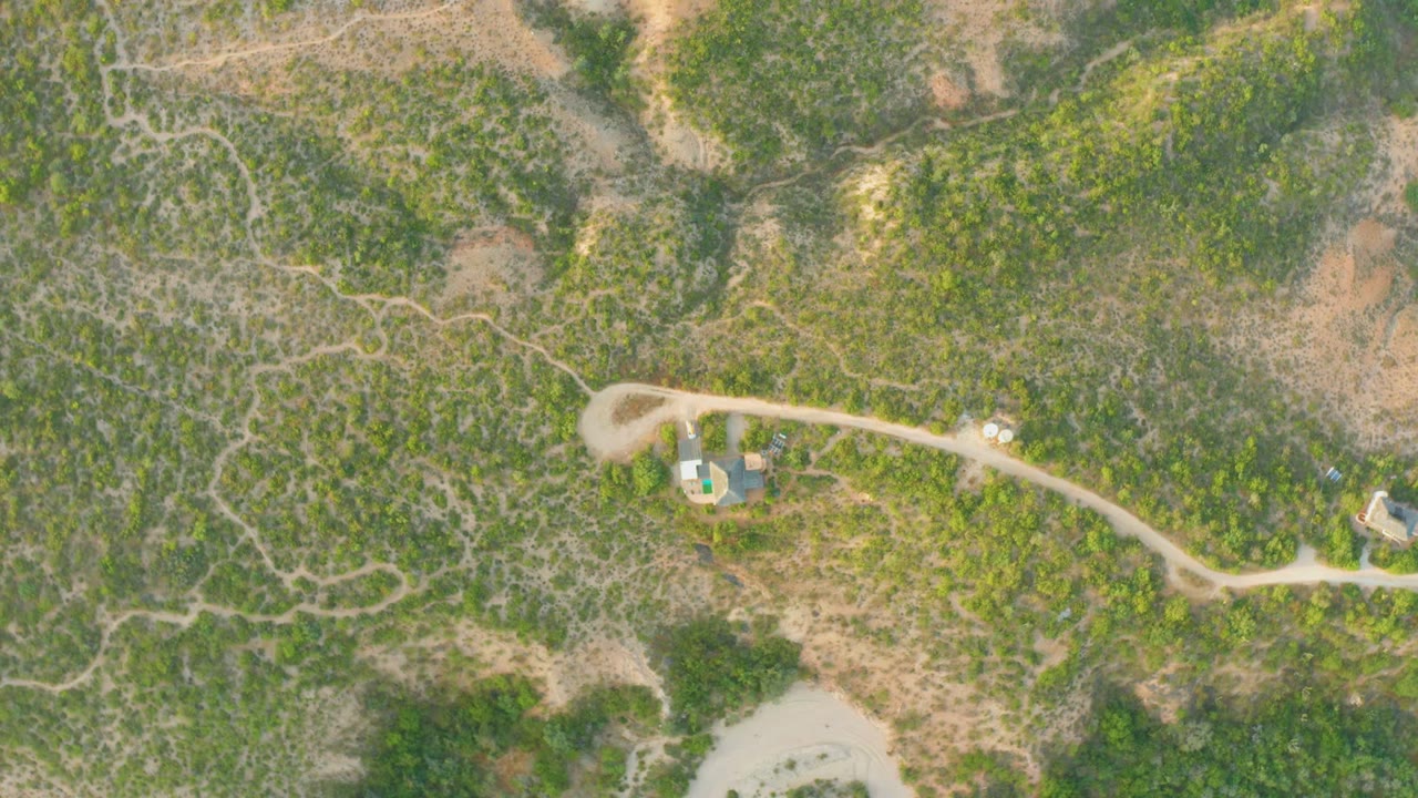 Overhead aerial frame in Cabo Pulmo, Baja California Sur showing a small house beside a pale dirt road, scrub vegetation, dry earth, and no visible people.