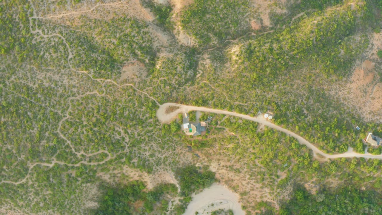 Aerial view of rural terrain with a house compound and winding dirt road.