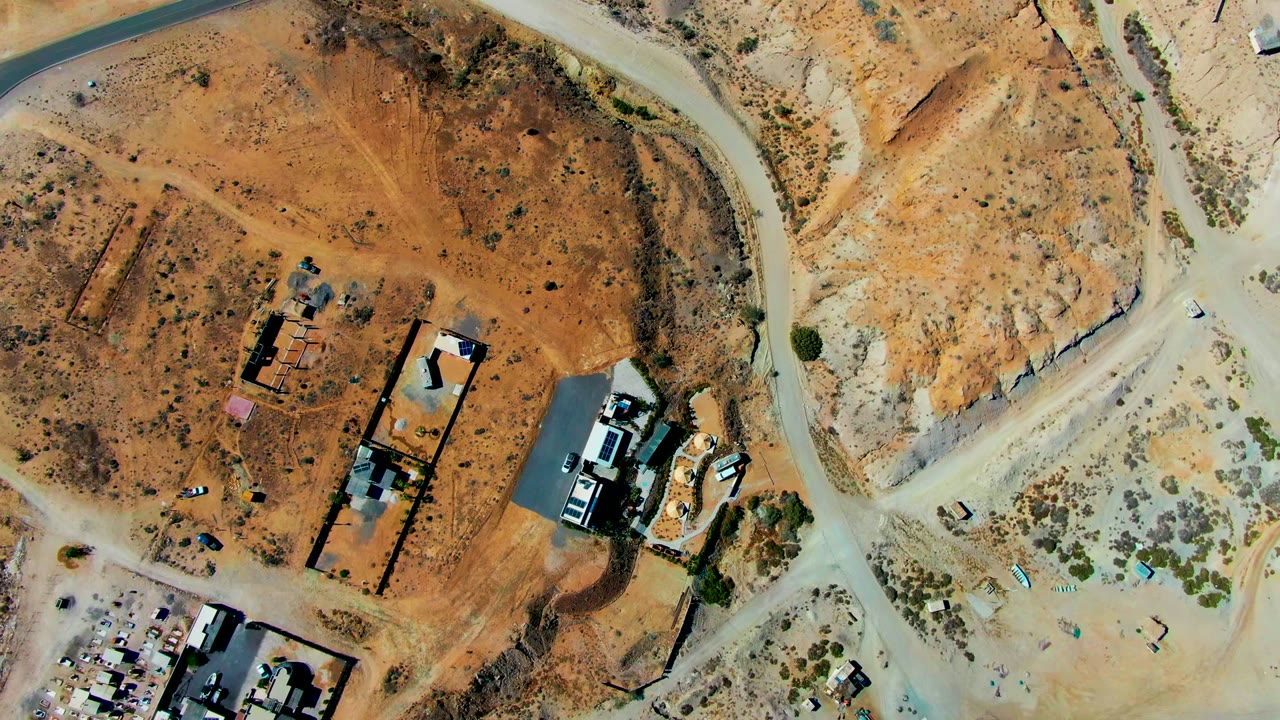Top-down aerial frame over San Juanico, Baja California Sur, showing sandy desert roads, sparse scrub, scattered structures, vehicles, and no visible people at the start of the clip.