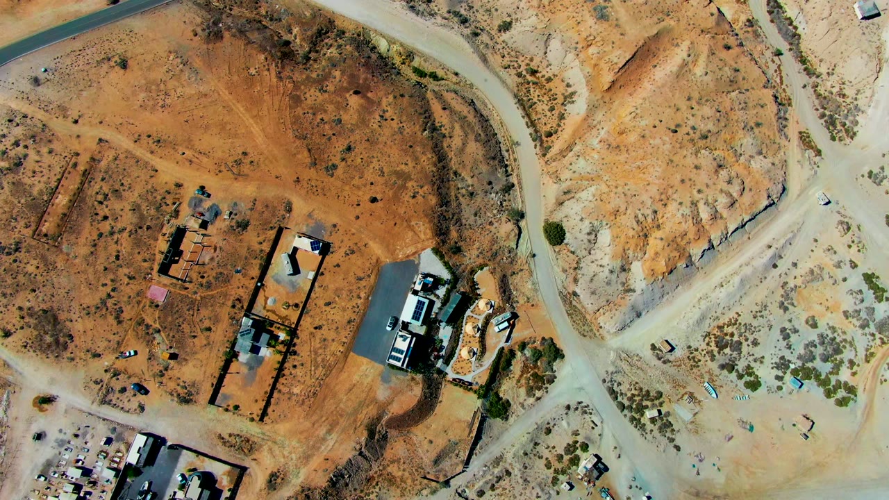 Aerial view of a white car near dirt roads and desert structures.