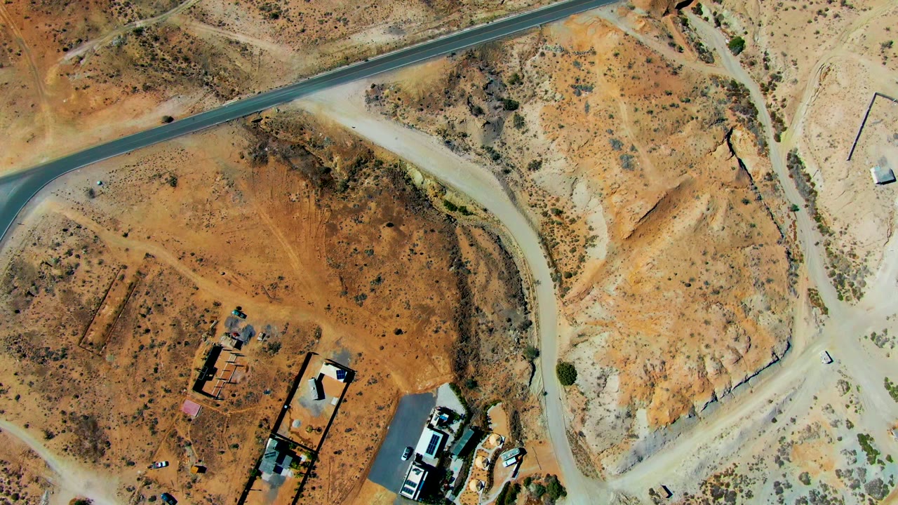 Aerial view of a car farther along a paved curve through desert ground.