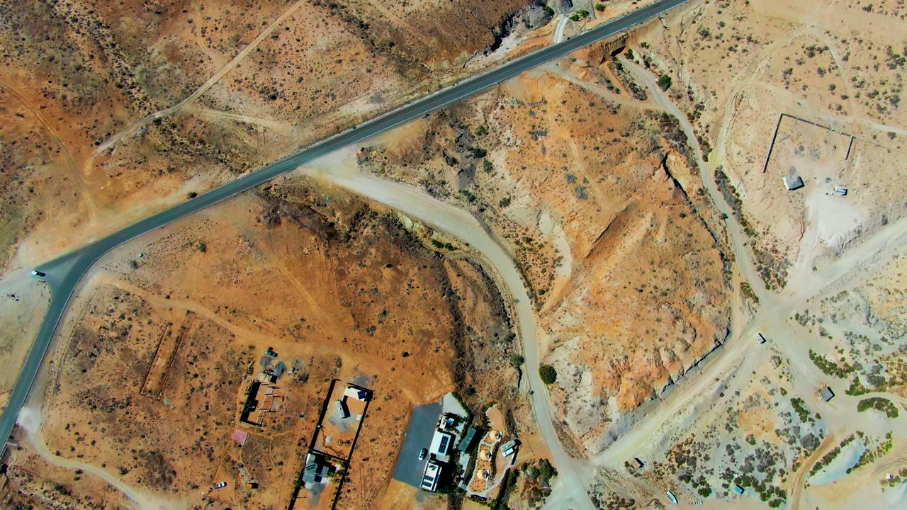 Aerial frame of a runway diagonal, dirt tracks, desert scrub, and small structures.