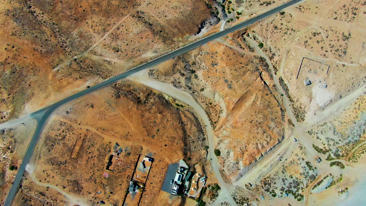 Diagonal paved road across sandy desert with a small vehicle near the lower road edge.