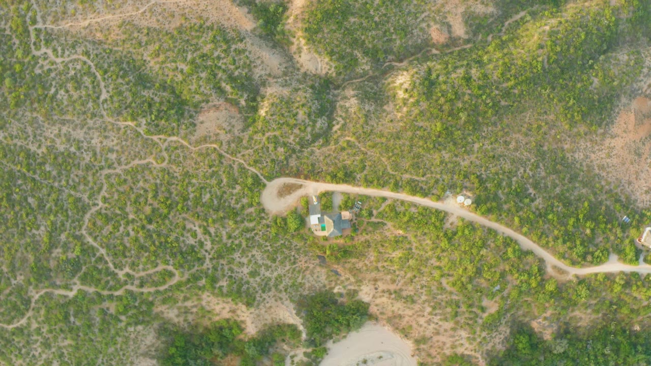 Aerial view of the same winding dirt road and brush-covered hillside.