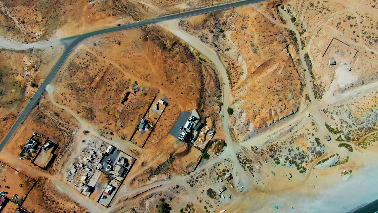 Overhead view of arid site with road, buildings, and beach water