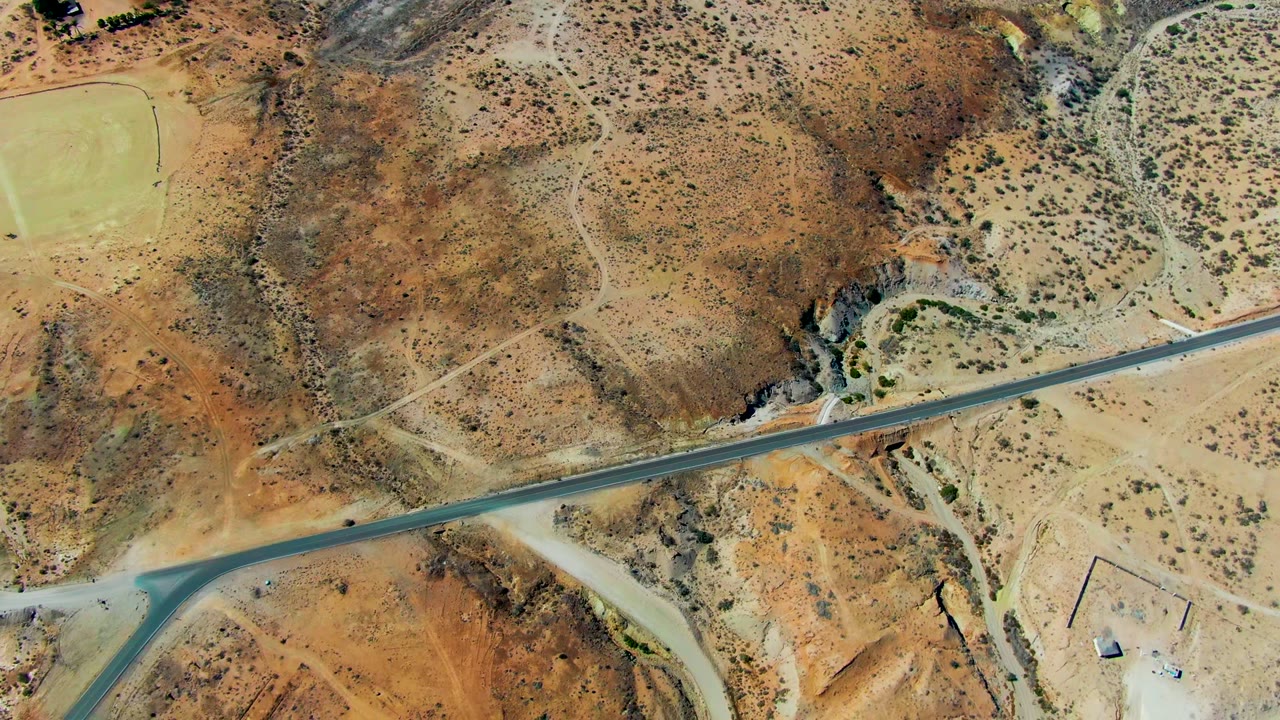Top-down aerial frame over San Juanico, Baja California Sur showing a paved runway crossing sandy desert hills, dirt tracks, sparse shrubs, and no visible people.