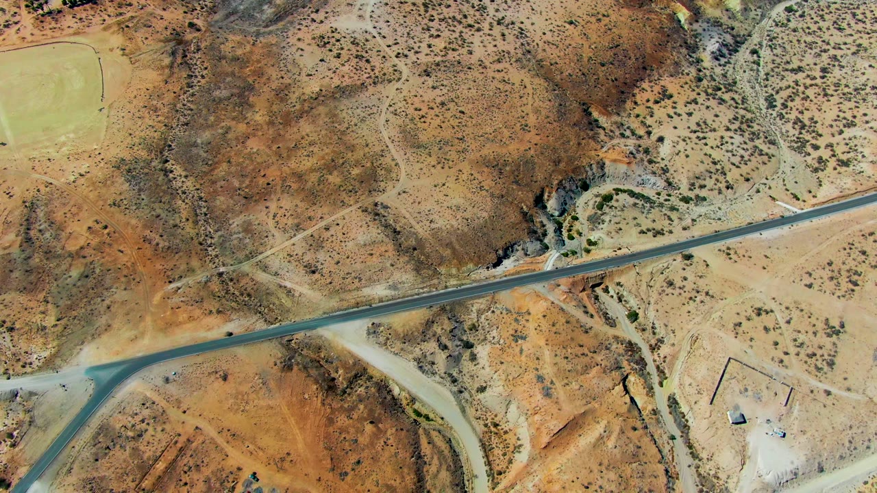 High aerial frame over San Juanico, Baja California Sur showing the runway stretching diagonally past pale sand, orange slopes, scrub patches, and no visible people.