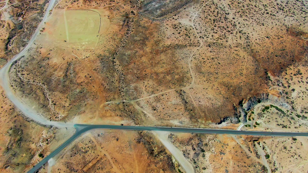 Overhead view of a road through dry desert terrain in San Juanico, Baja California Sur, with a small vehicle near the left side and no visible people.