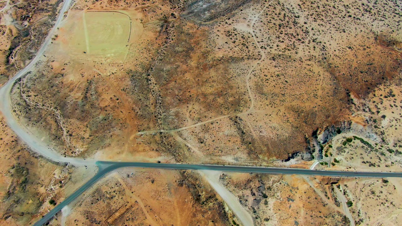Aerial view of a desert road crossing scrubland and a green field.