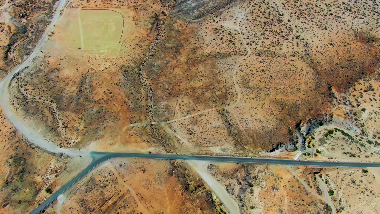 Overhead San Juanico desert view with a straight road segment crossing scrubby brown terrain, intersecting dirt tracks, and no visible people.
