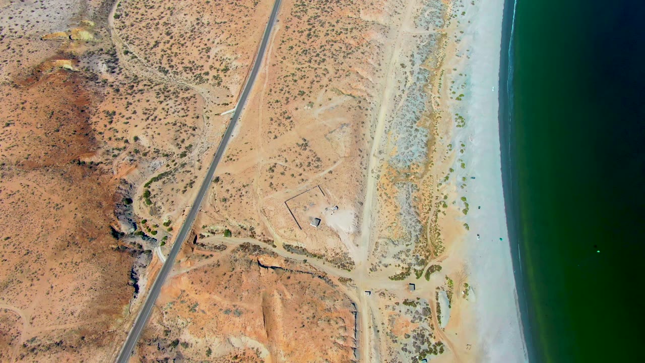 Aerial view of a coast road crossing dry desert above a sandy shore.