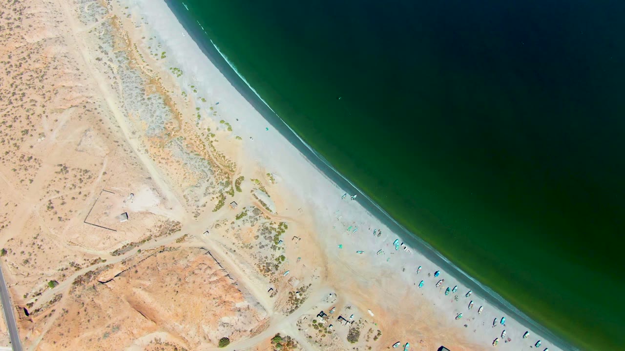 Aerial shoreline with desert terrain, beach umbrellas, and dark green water.