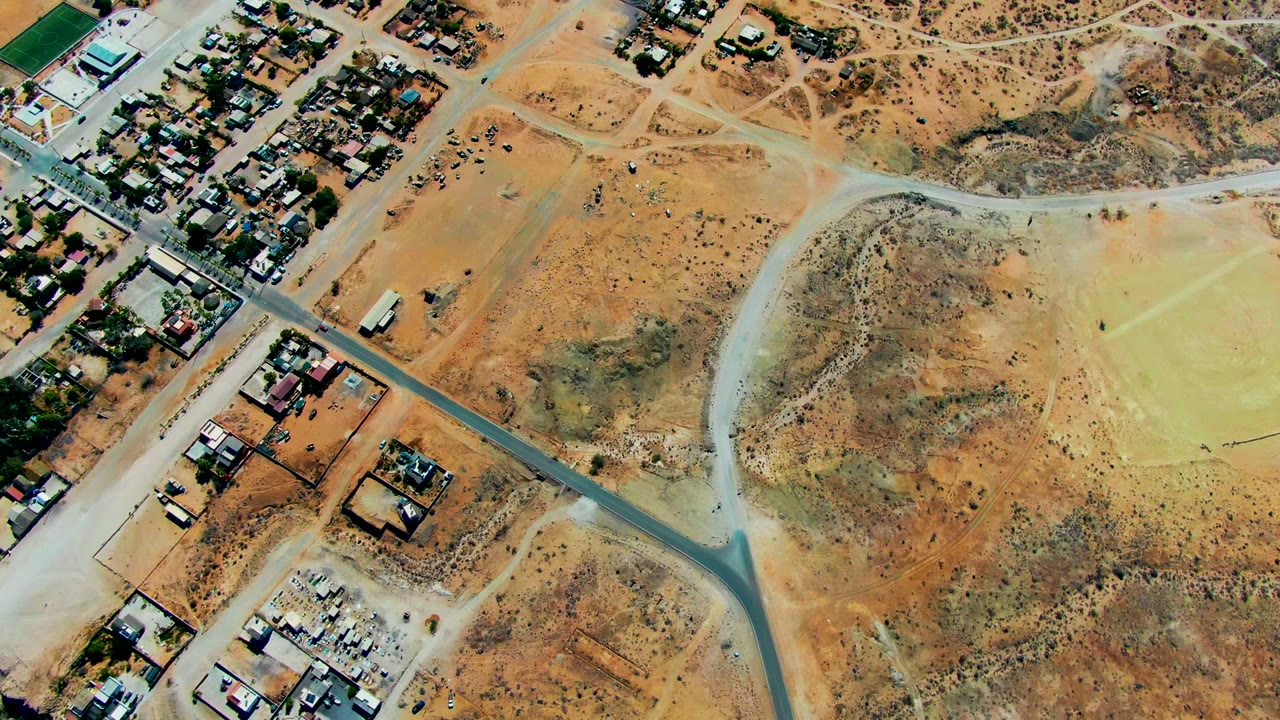 Aerial view of a paved road crossing dry lots with houses and scrubland.