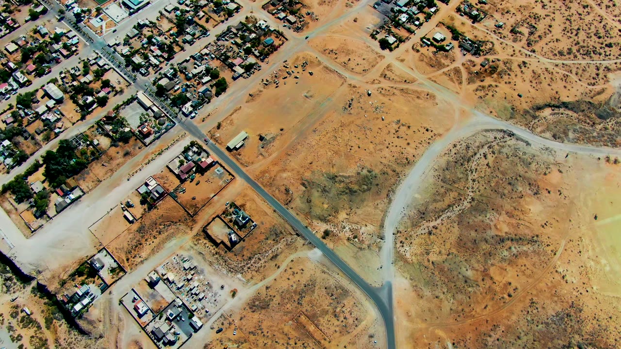 Aerial frame over San Juanico showing residential blocks near dry hills, intersecting roads, a pale field area, and no visible people.
