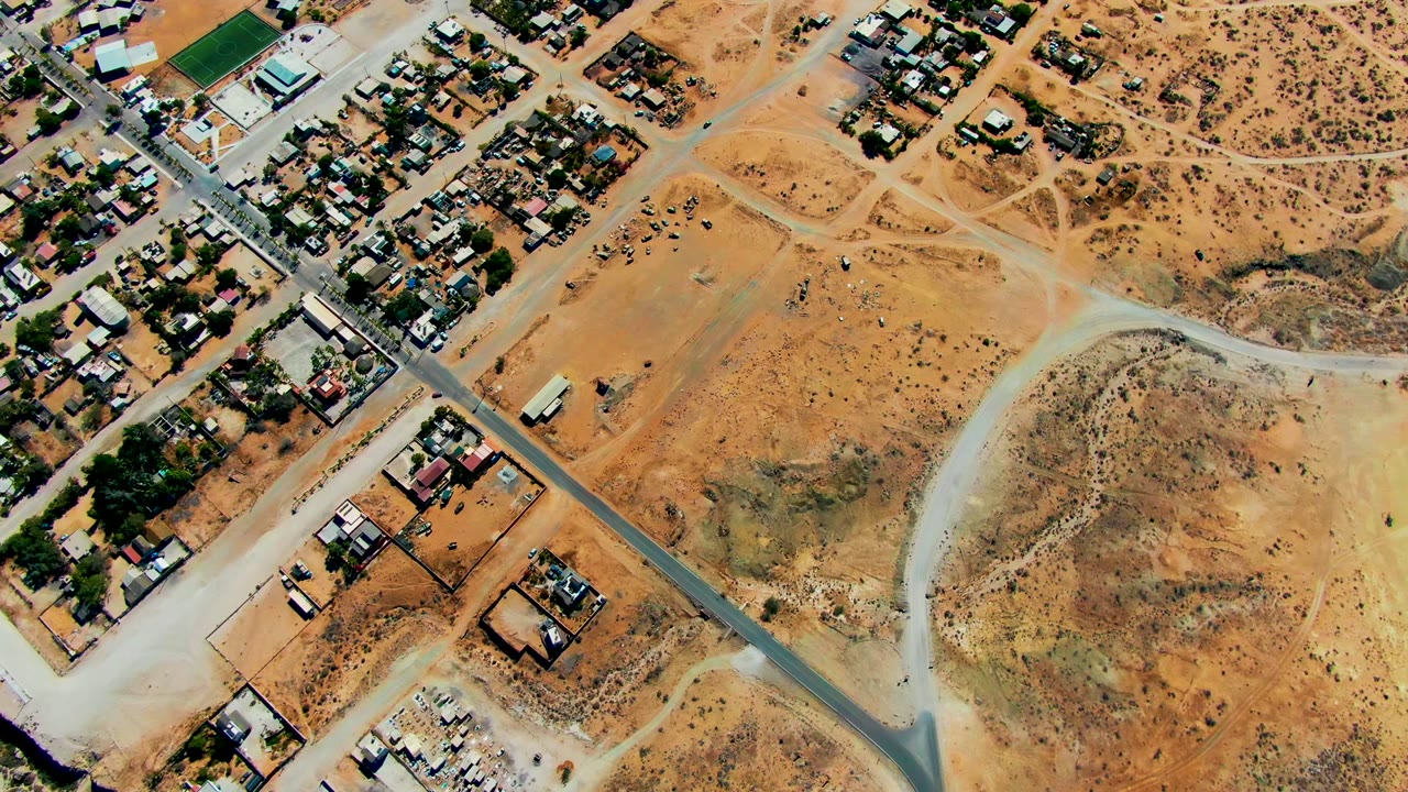 High aerial frame over San Juanico, Baja California Sur, showing scattered houses, pale dirt roads, a paved road, scrubby desert ground, and no visible people.