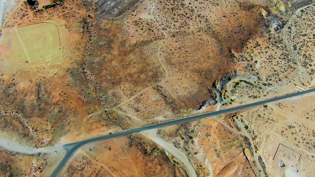 Paved road crossing arid scrubland near a dirt intersection.