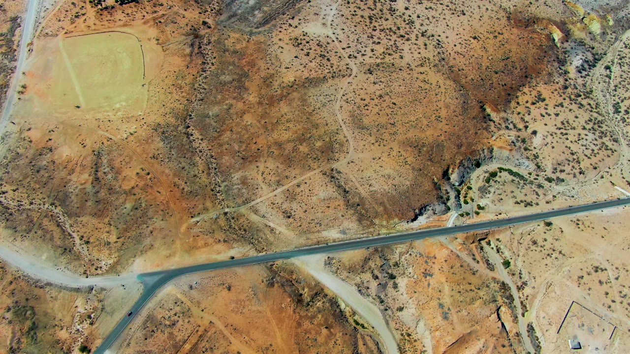 Aerial desert road with scrub hills and pale dirt paths.