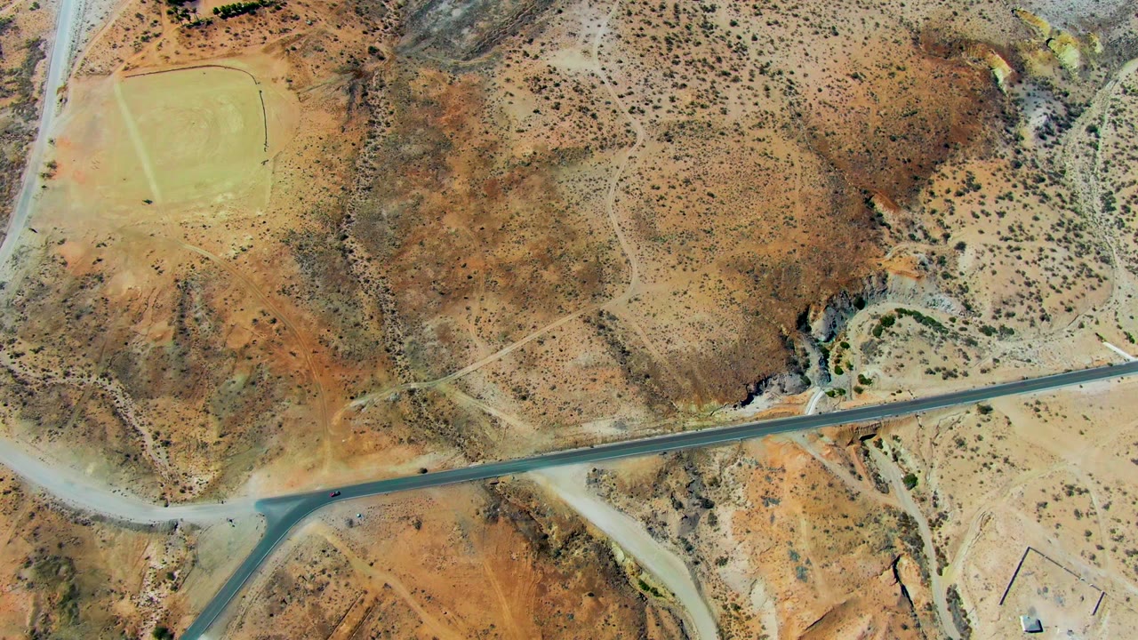 Aerial desert road crossing near a pale runway area.