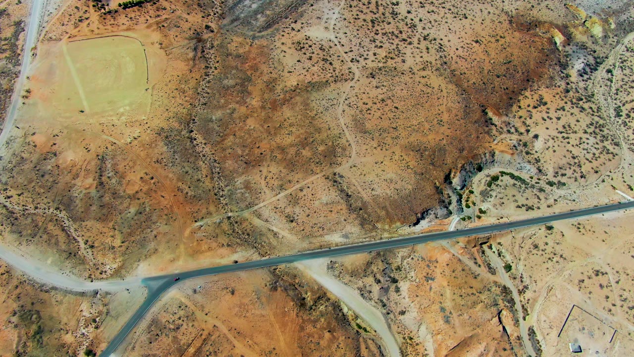 Mid-clip aerial frame in San Juanico, Baja California Sur showing the road corridor across scrubby brown terrain, the runway area at upper left, and no visible people.