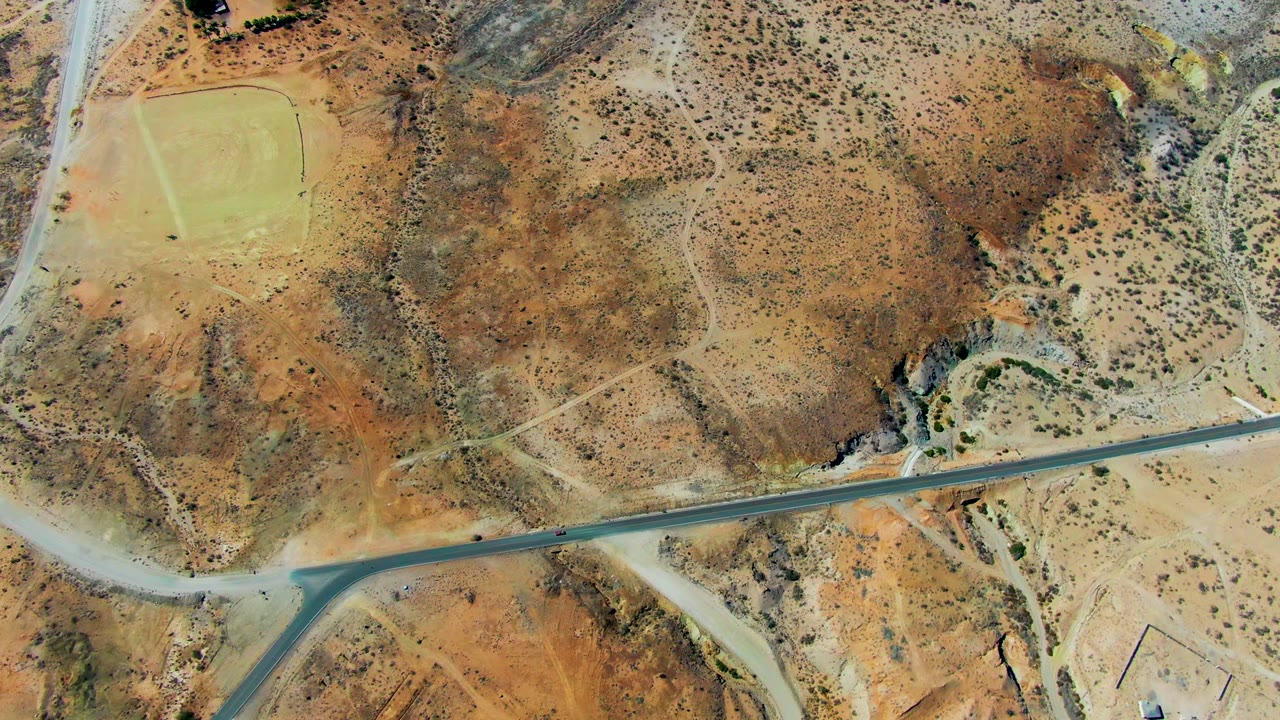 Small vehicle moving along a paved road in arid terrain