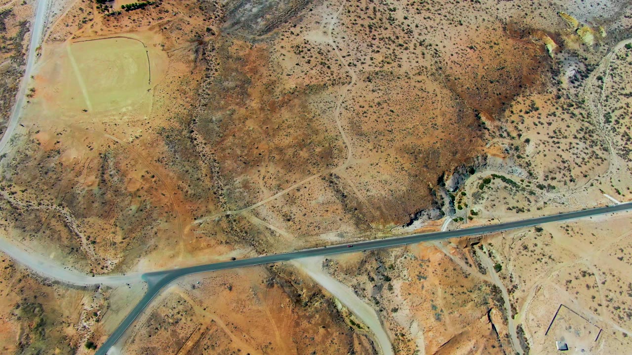 Aerial view of a car on a desert road below scrub-covered hills.