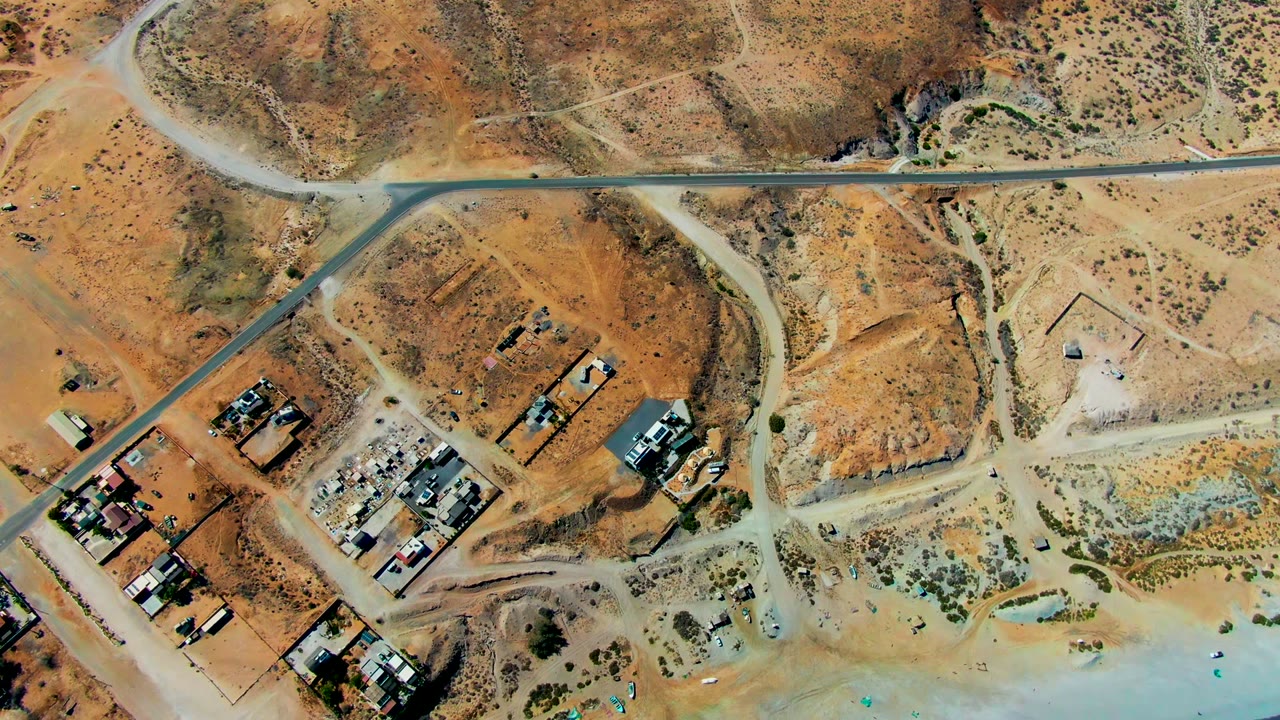 Aerial view of paved road crossing dry terrain near buildings