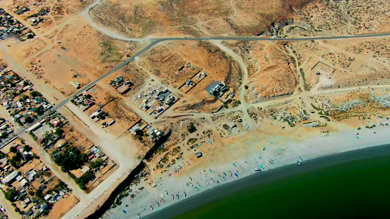 Overhead view of desert lots, beach access roads, sandy shore, and green water.