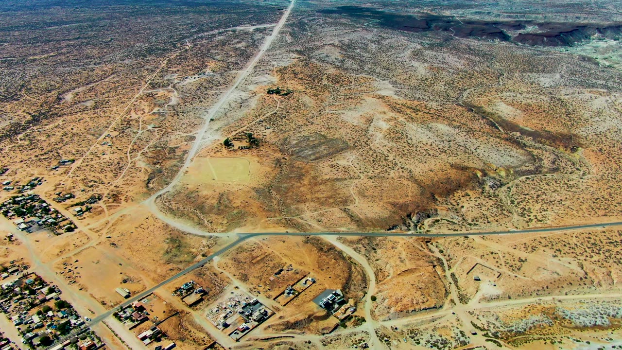 Opening aerial frame over San Juanico, Baja California Sur, showing tan desert scrub, intersecting roads, scattered settlement buildings near the lower edge, and no visible people.